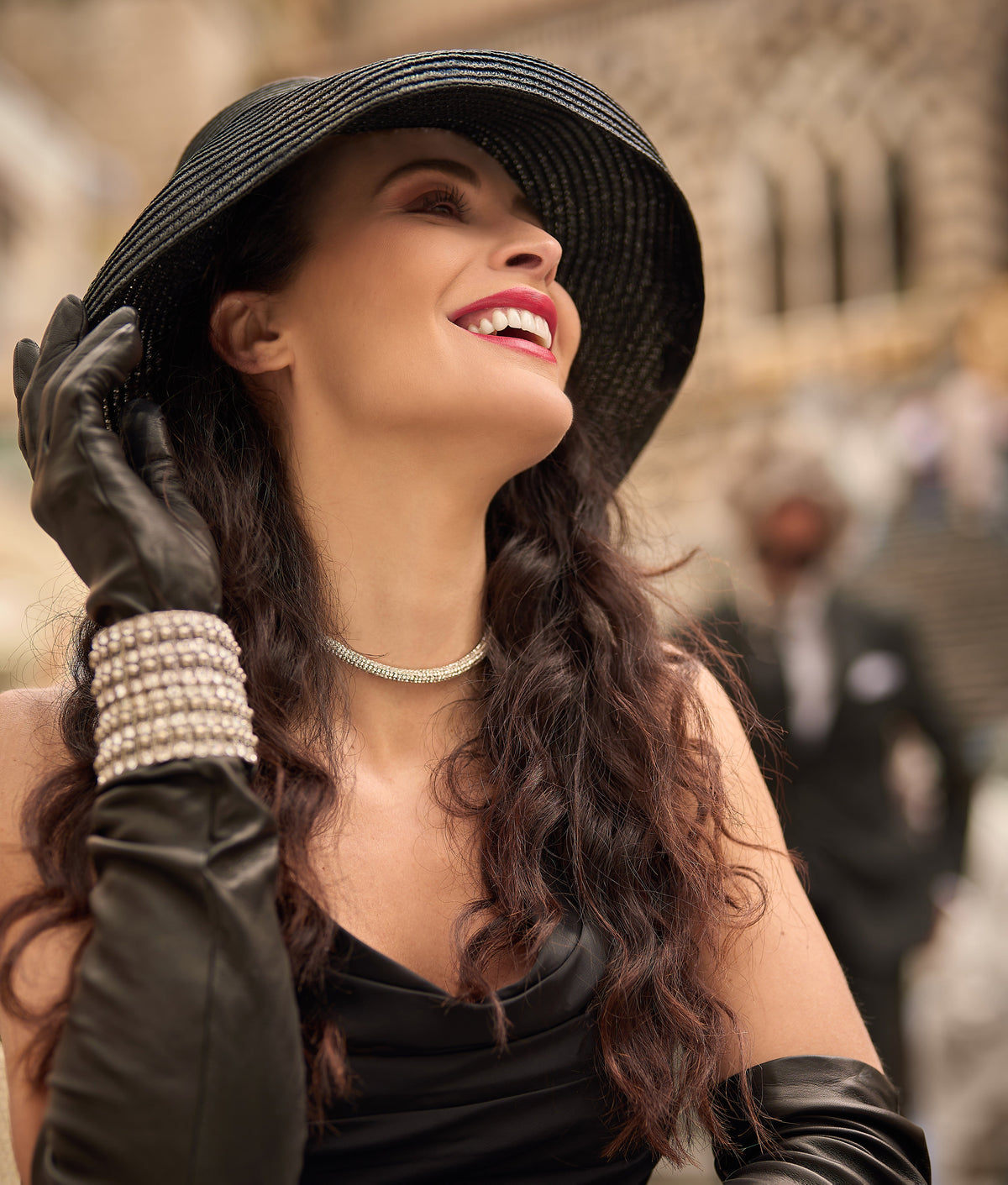 Elegant woman wearing black nappa leather opera gloves, styled with a wide-brimmed hat and pearl accessories, exuding luxury.