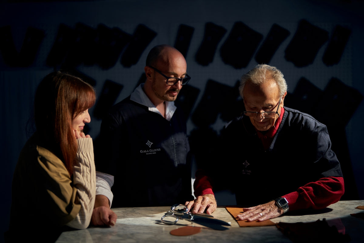 Artisans collaborating in a workshop, examining premium leather pieces for Gala Gloves, showcasing Italian craftsmanship.
