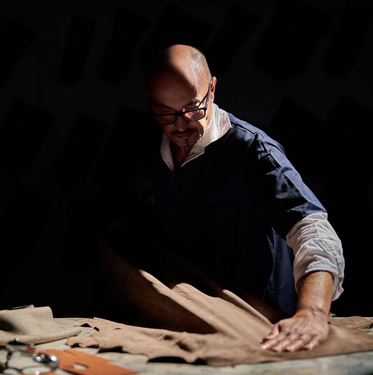 Alessandro Pellone carefully inspecting soft brown leather, showcasing meticulous attention to detail in Italian glove craftsmanship.
