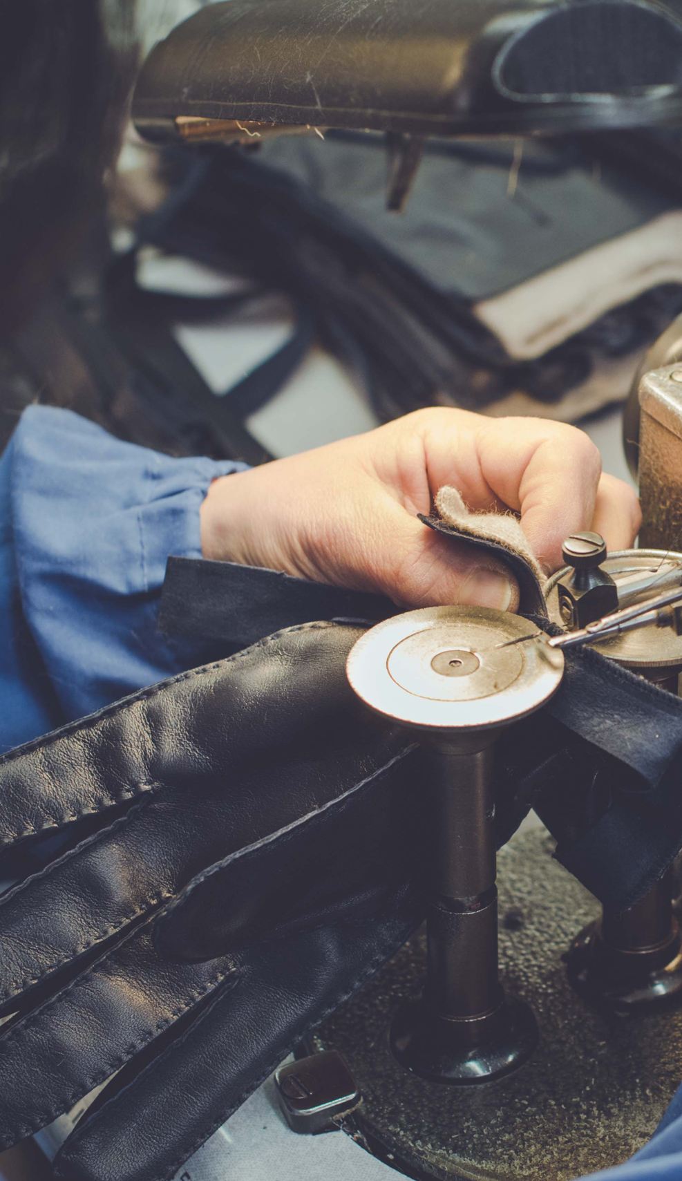 Artisan hand-sewing black leather gloves using a vintage machine, showcasing meticulous Italian craftsmanship and attention to detail.